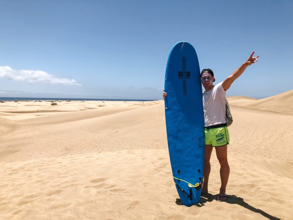 Surfer drzi modry surf na dunach Maspalomas